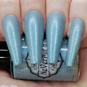 A close-up image of long coffin shaped fingernails painted with a light blue nail polish, featuring a reflective glitter finish, shown without flash
