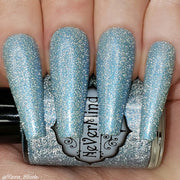 A close-up image of long coffin shaped fingernails painted with a light blue nail polish, featuring a reflective glitter finish.