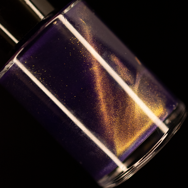 Image of a nail polish bottle on a lack background. The nail polish is a purple with gold magnetic effects.