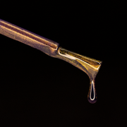 Image of a nail polish brush on a lack background. The brush is dripping nail polish. The nail polish is a purple with gold magnetic effects.