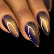 A close-up image of a person's fingernails painted with a purple and gold magnetic nail polish, showing a gradient from purple to gold with a magnetic effect.