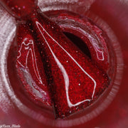 Brush immersed in vibrant red reflective glittery nail polish with a sparkle effect