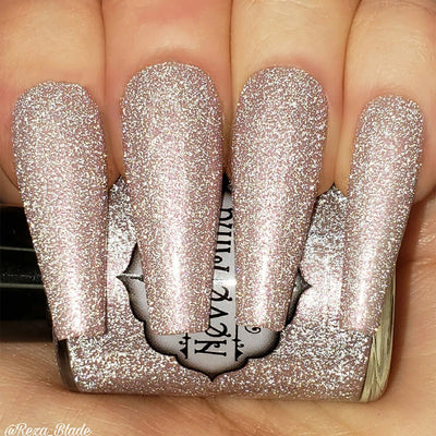 A close-up image of long coffin shaped fingernails painted with a light pink nail polish, featuring a reflective glitter finish.