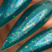 Close-up of stiletto-shaped nails painted with shimmery teal nail polish featuring multicolored flecks.